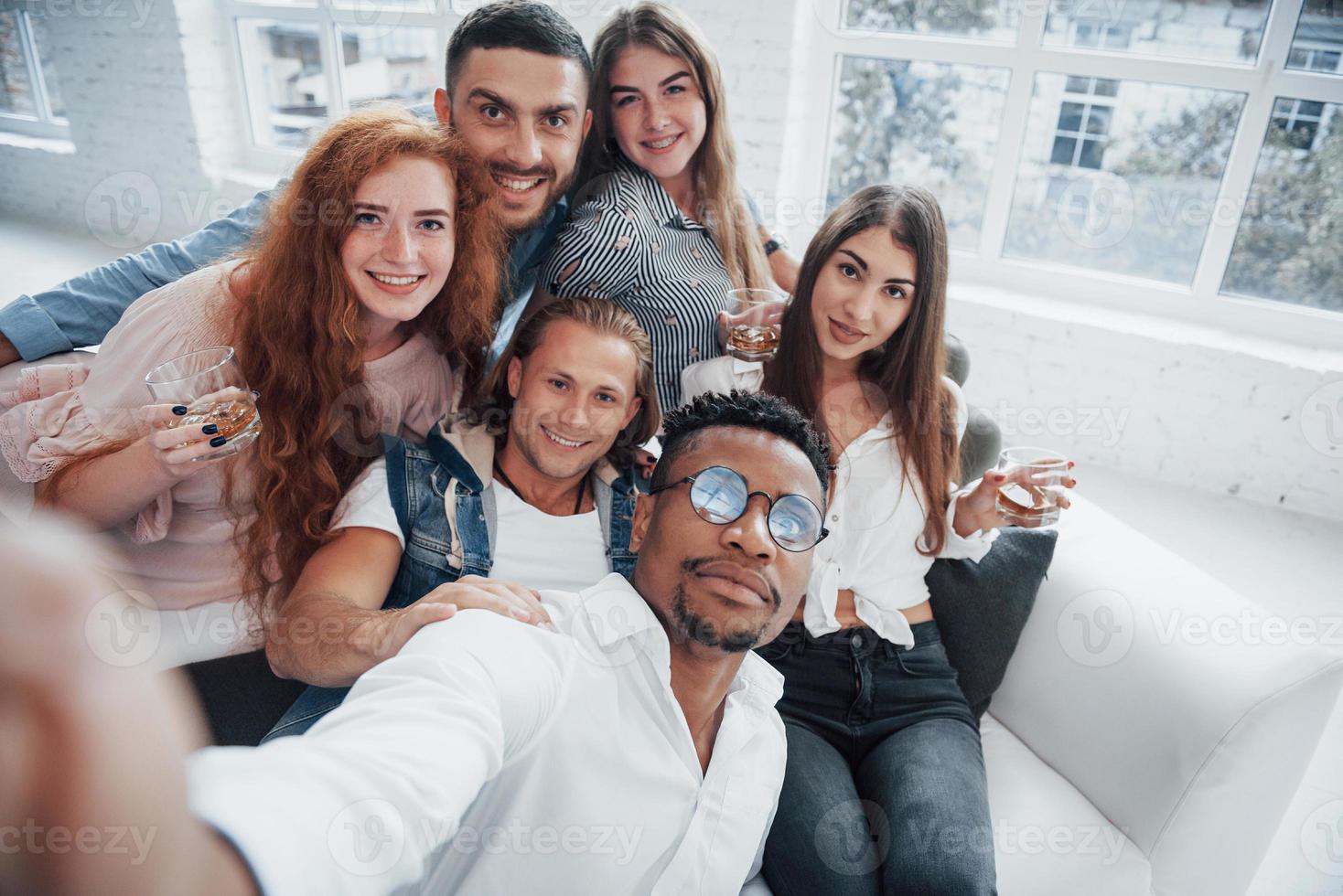 Need to capture this moment. Cheerful young friends having fun and drinking in the white interior photo