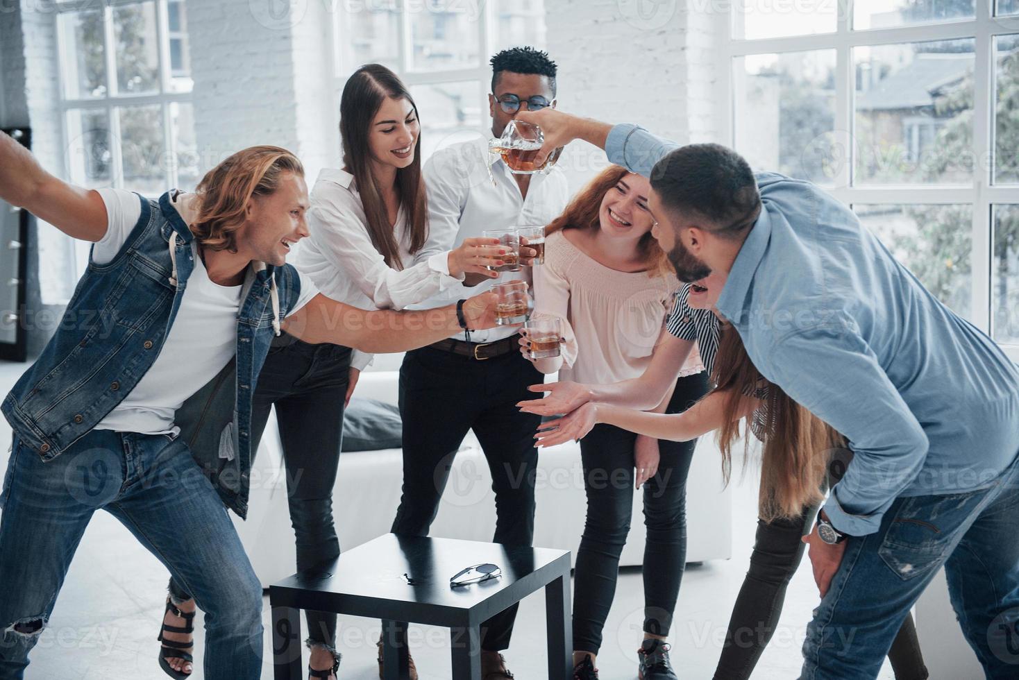 Alegres jóvenes amigos divirtiéndose y bebiendo en el interior blanco foto