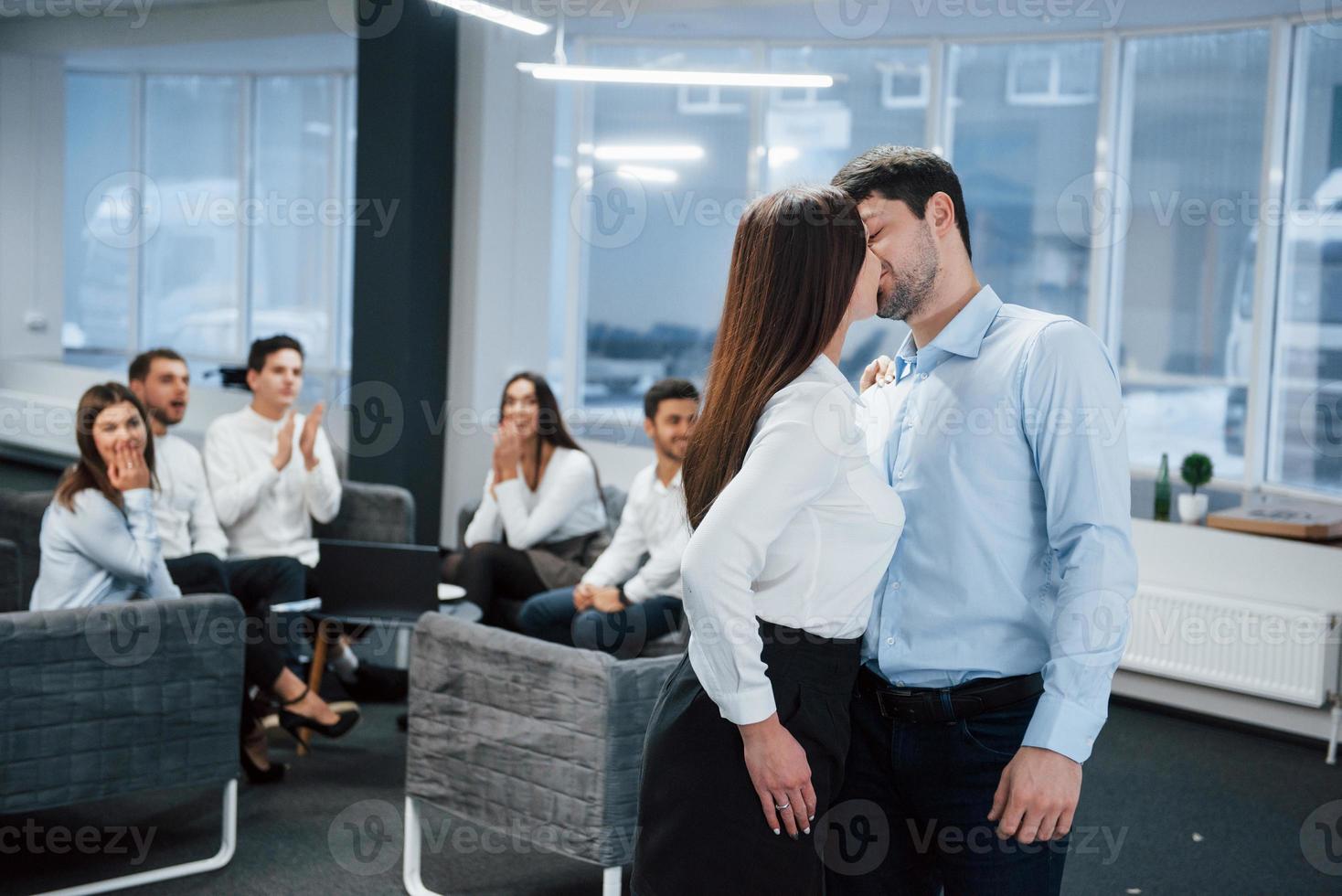 Spontaneous lovely kiss between two employees shocked other office workers photo