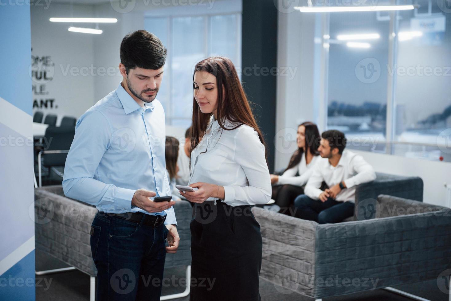 dispositivos modernos en concepto de negocio. Dos trabajadores de oficina con ropa clásica hablando frente a los empleados. foto