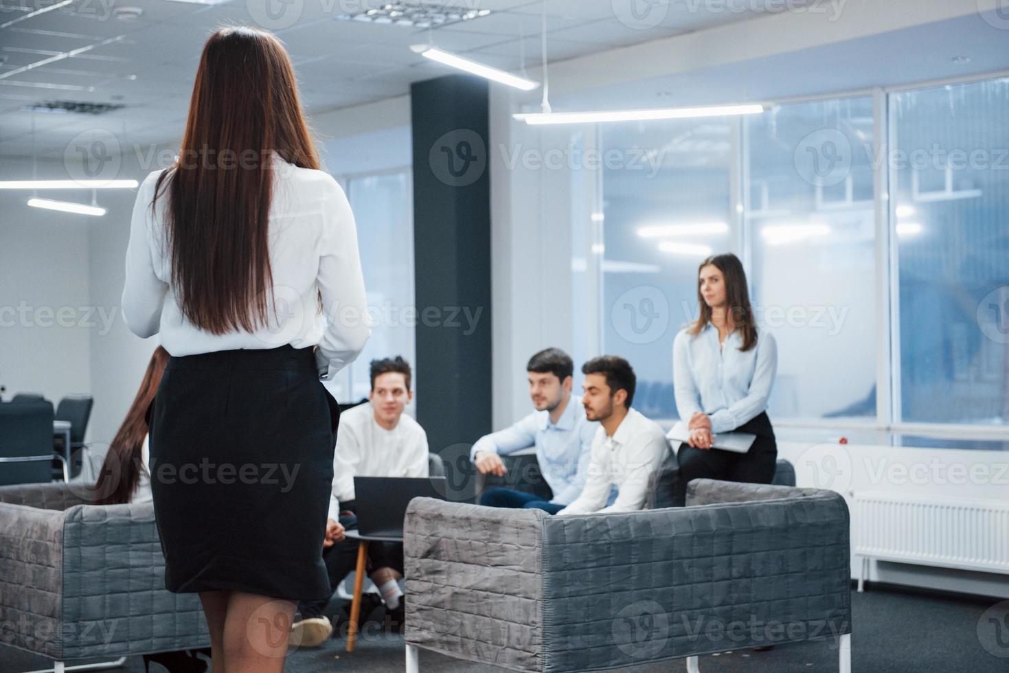 Girl in skirt is walking to the employees that sitting on sofa and waiting photo