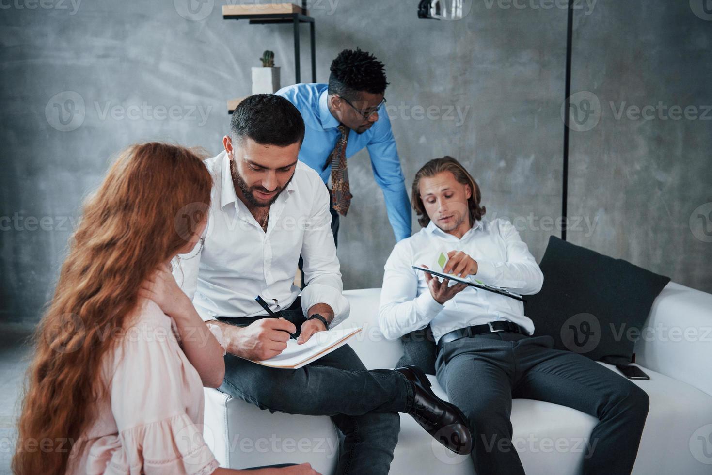 trabajar con listas de información. Grupo de oficinistas multirraciales en ropa formal hablando de tareas y planes. foto