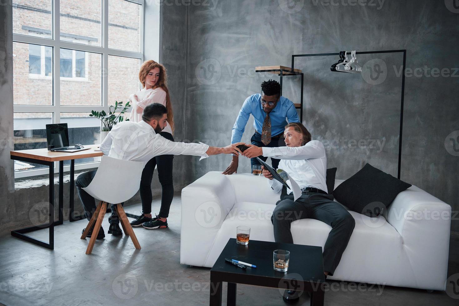 las tecnologías modernas se han convertido en una parte integral del trabajo. Grupo de oficinistas multirraciales en ropa formal hablando de tareas y planes. foto