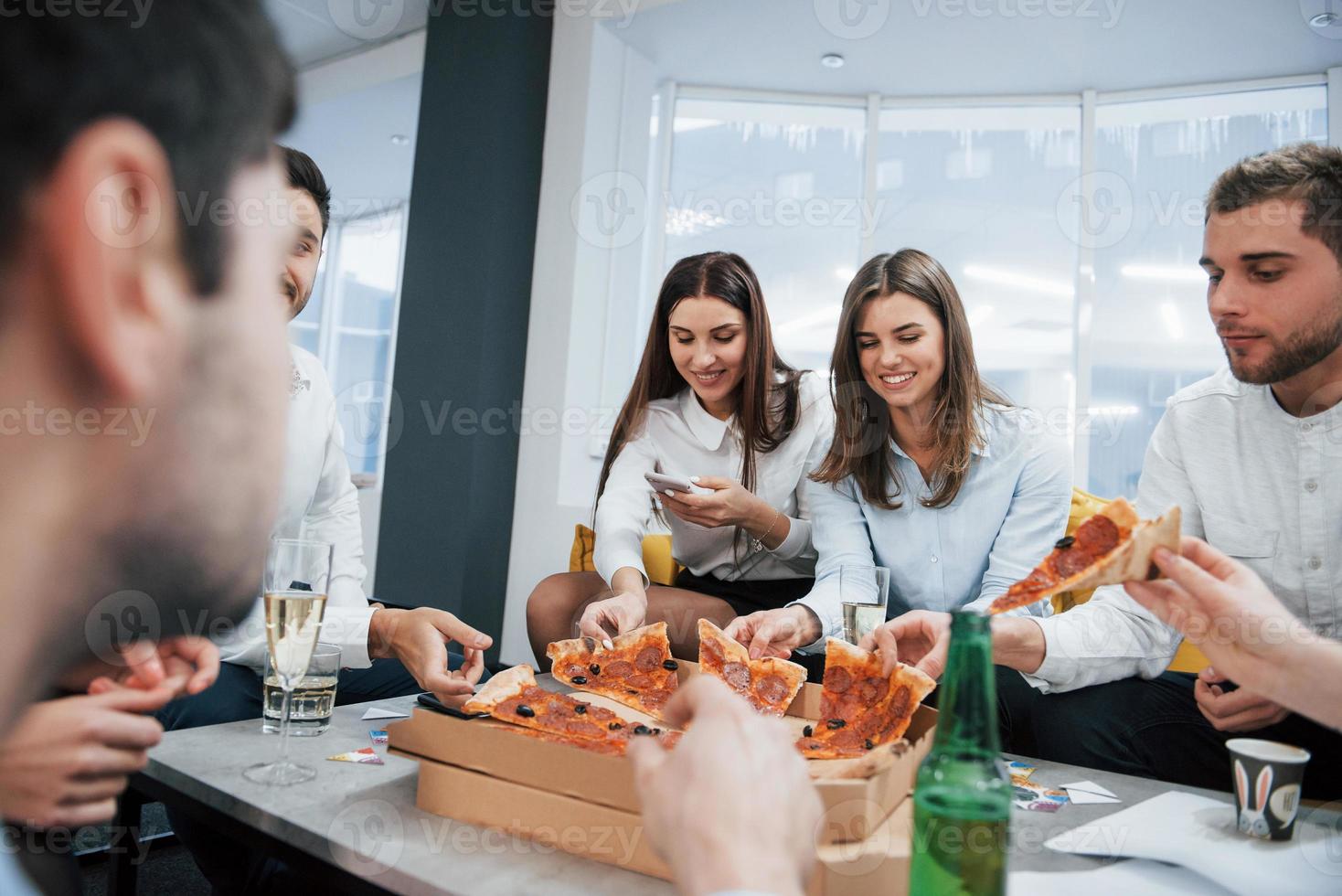 Having good time. Eating pizza. Celebrating successful deal. Young office workers sitting near the table with alcohol photo