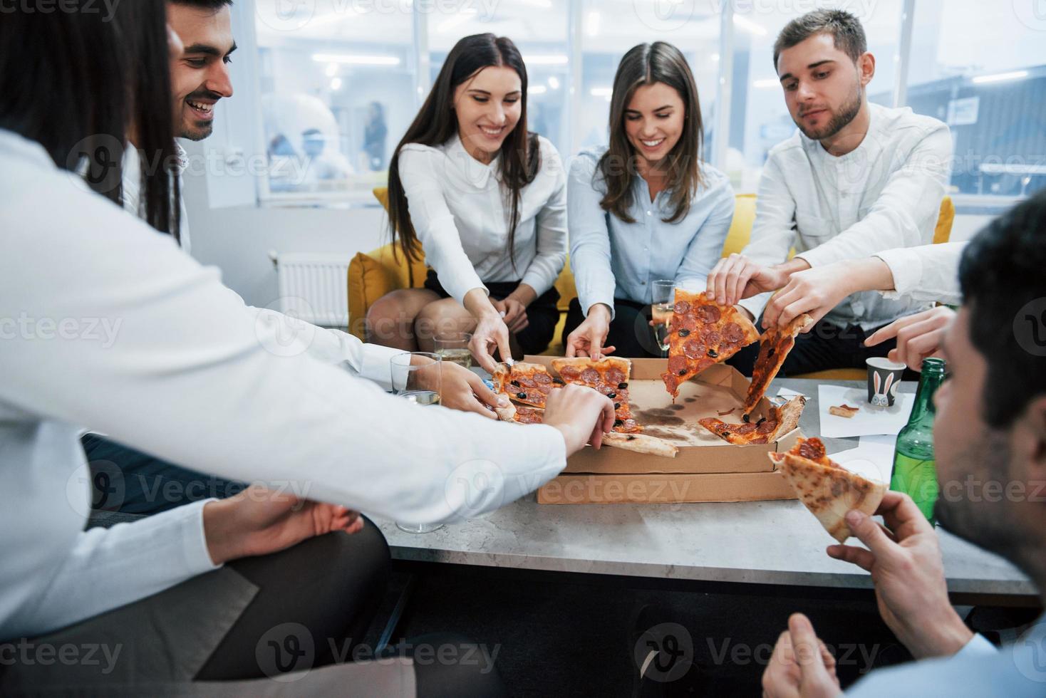 comiendo pizza. celebrando un trato exitoso. jóvenes trabajadores de oficina sentados cerca de la mesa con alcohol foto