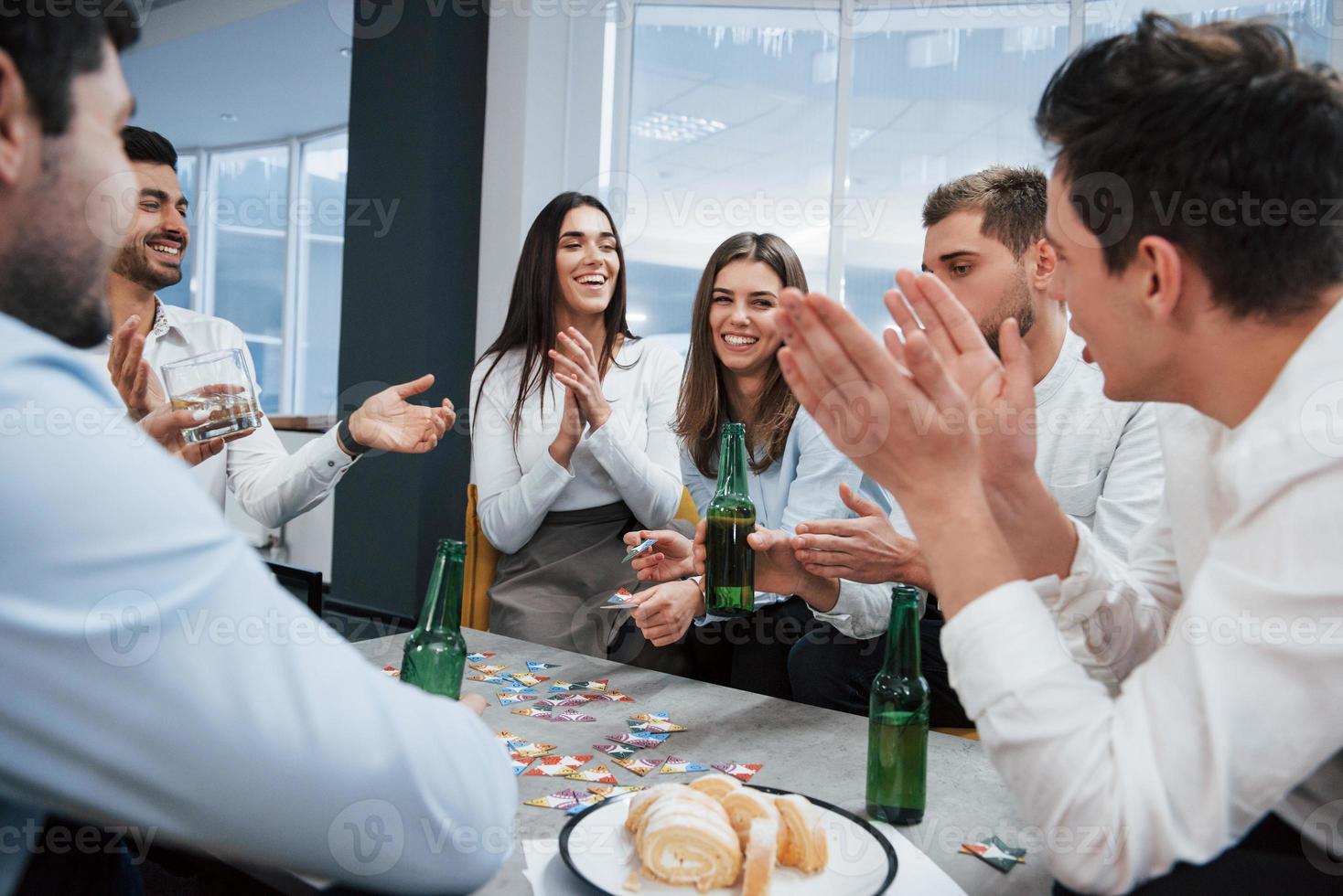 The winner is that girl. Celebrating successful deal. Young office workers sitting near the table with alcohol photo