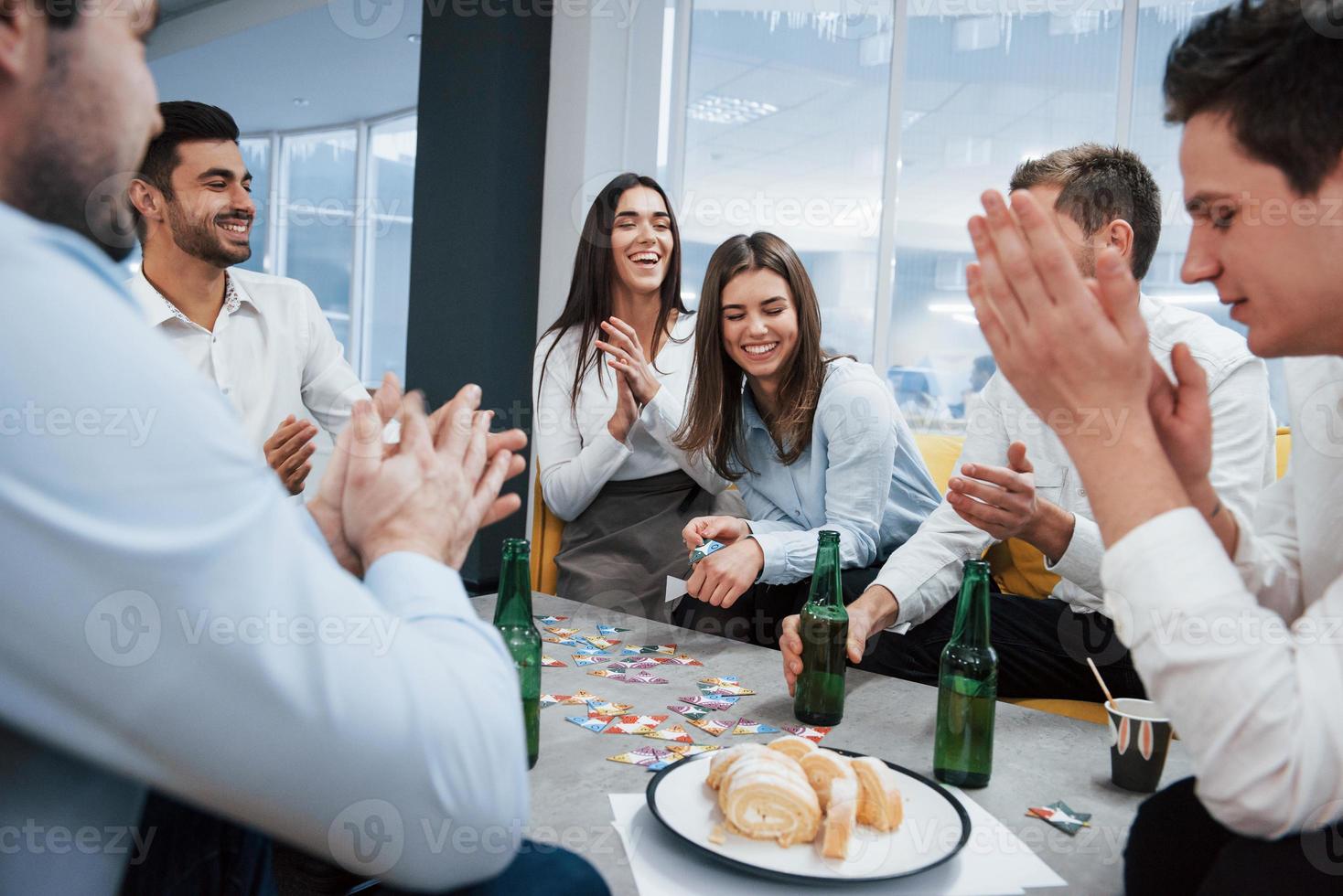 todo el mundo está sonriendo. celebrando un trato exitoso. jóvenes trabajadores de oficina sentados cerca de la mesa con alcohol foto