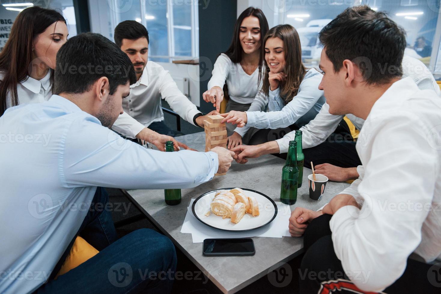 comida, taza y botellas. celebrando un trato exitoso. jóvenes trabajadores de oficina sentados cerca de la mesa con alcohol foto