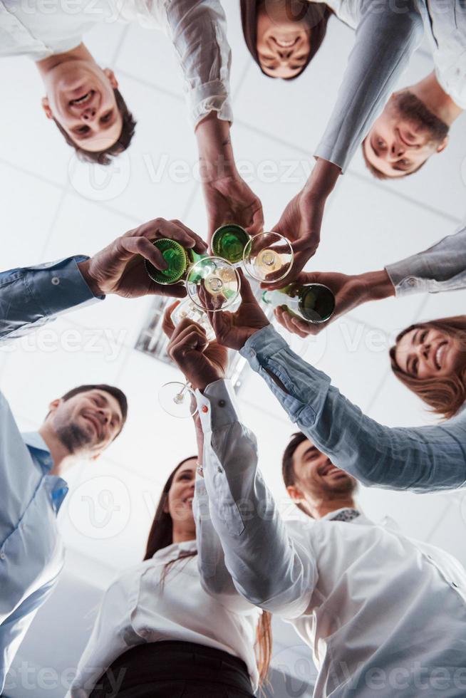 Vertical photo. View from below. Knocking glasses in the office. Celebrating success photo