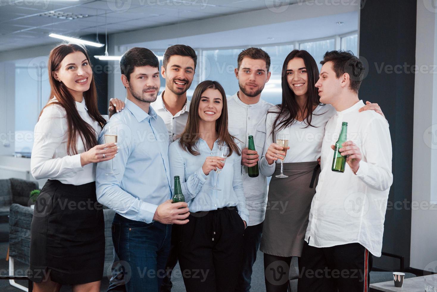 Celebrating of success. Photo of young team in classical clothes holding drinks in the modern good lighted office