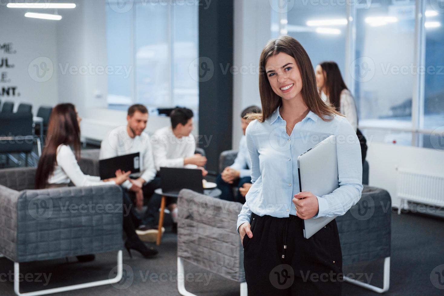 mirada satisfecha. Retrato de joven se encuentra en la oficina con empleados en segundo plano. foto