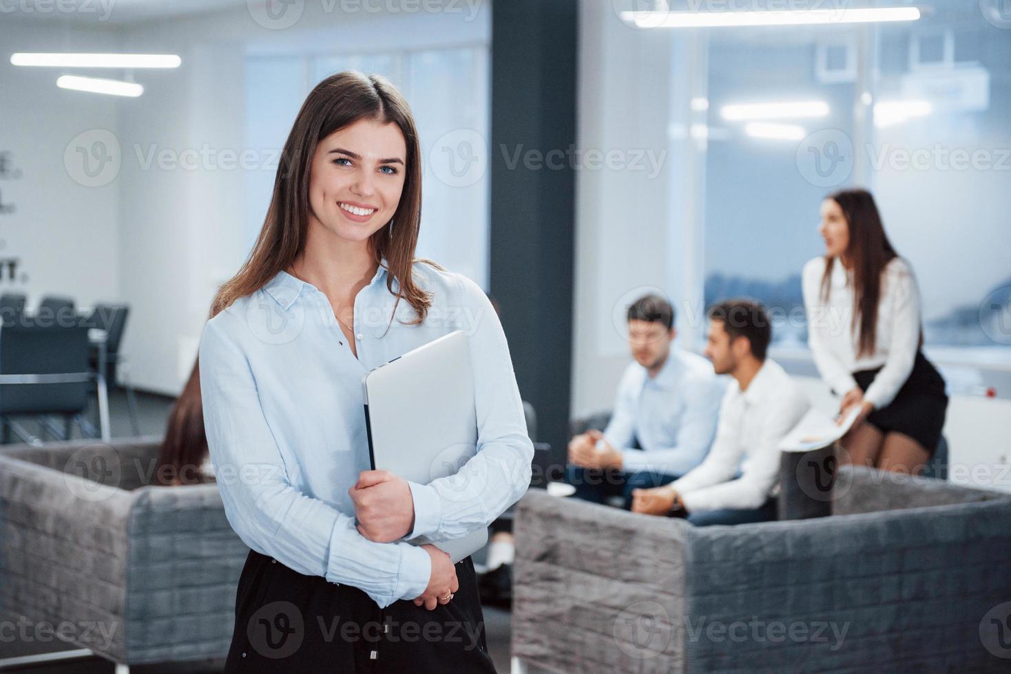 mujer hermosa. Retrato de joven se encuentra en la oficina con empleados en segundo plano. foto