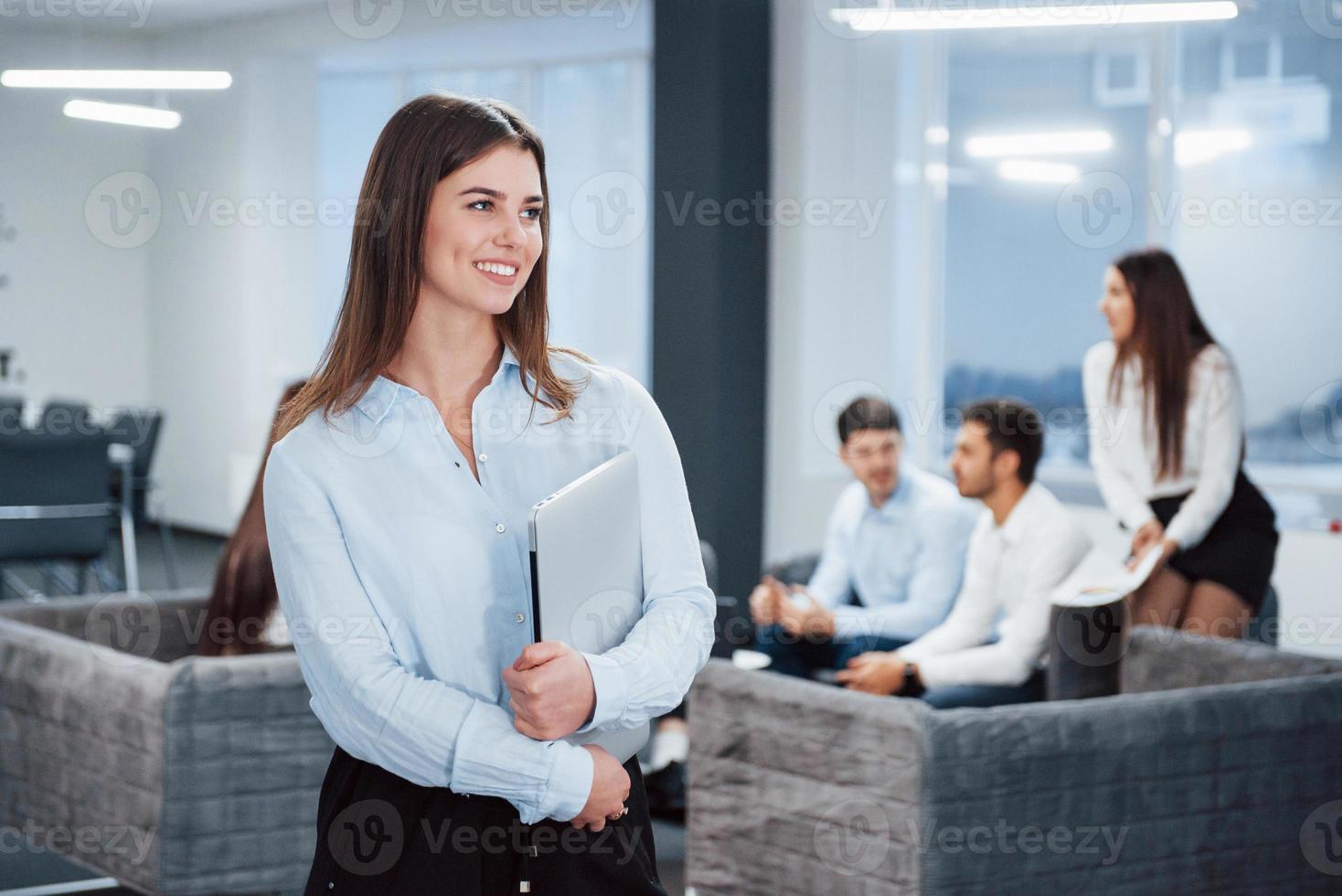 buena iluminación. Retrato de joven se encuentra en la oficina con empleados en segundo plano. foto