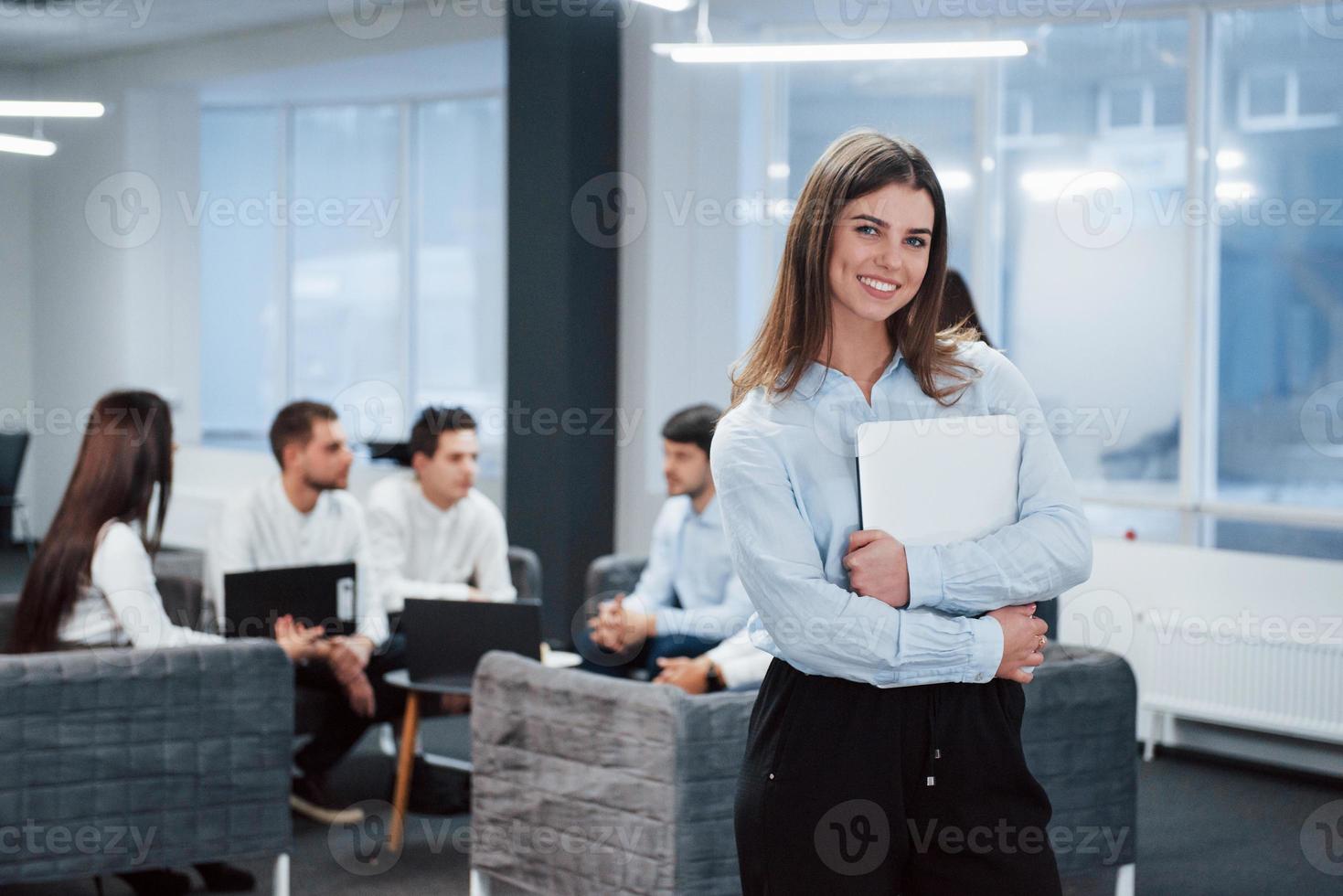 la mujer tiene tiempo de descanso. Retrato de joven se encuentra en la oficina con empleados en segundo plano. foto