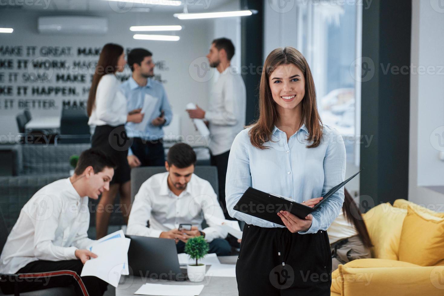 Focused photo. Portrait of young girl stands in the office with employees at background photo