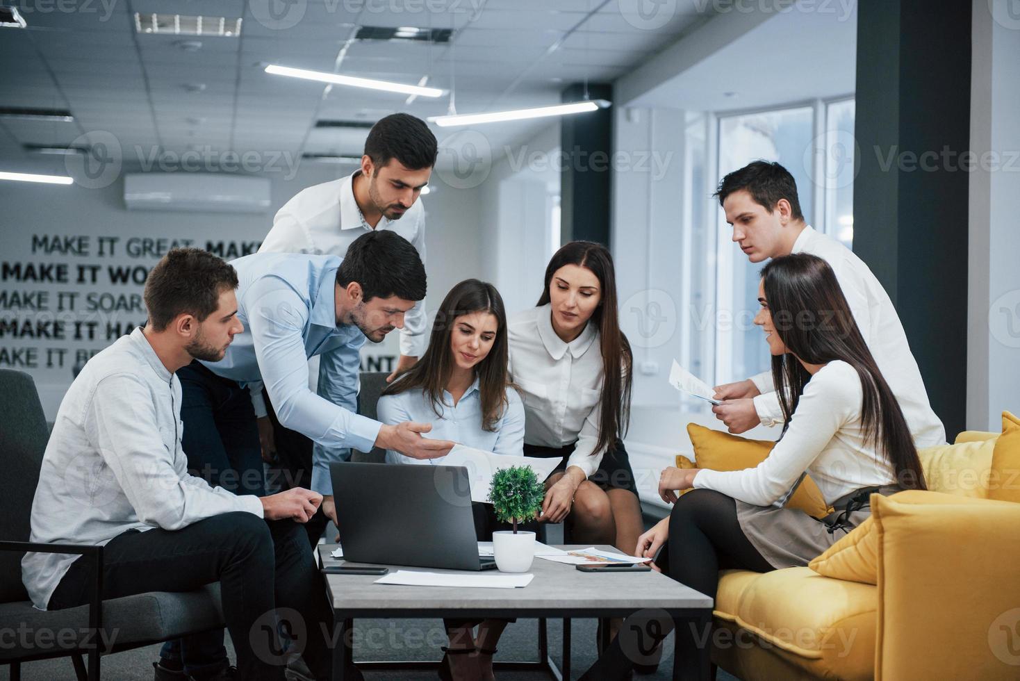 Guy shows document to a girl. Group of young freelancers in the office have conversation and working photo