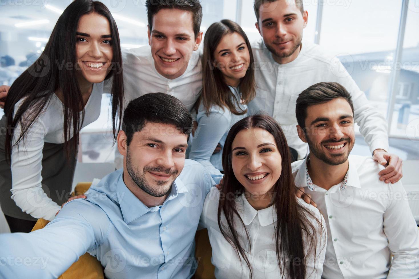 foto del teléfono. Equipo joven haciendo selfie en ropa clásica en la moderna oficina bien iluminada