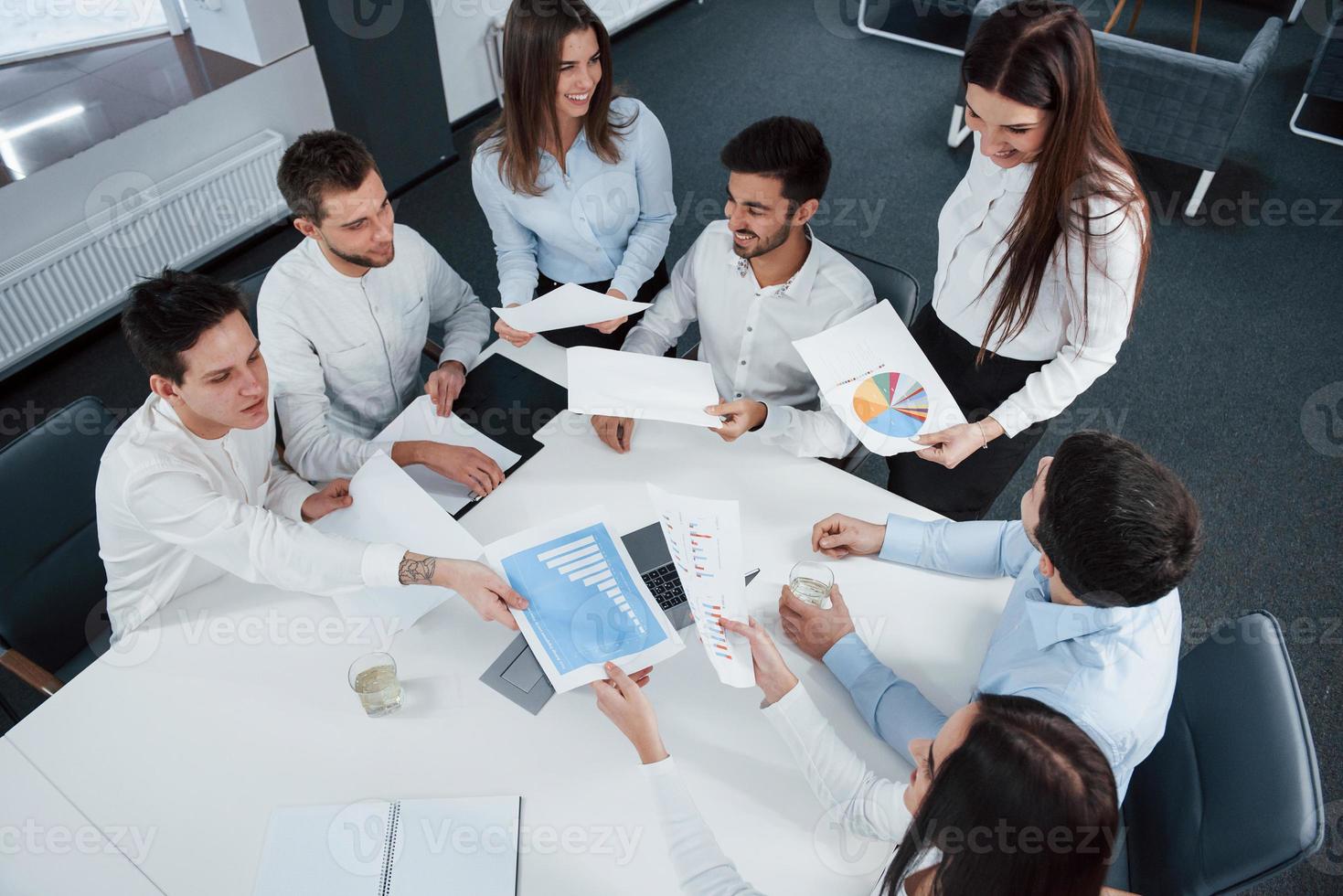 tan joven pero tan exitoso. Vista superior de los trabajadores de oficina en ropa clásica sentados cerca de la mesa usando una computadora portátil y documentos foto