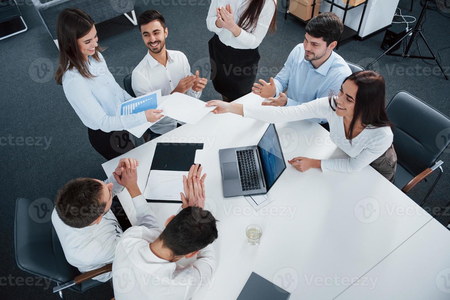 Happy people. Top view of office workers in classic wear sitting near the table using laptop and documents photo