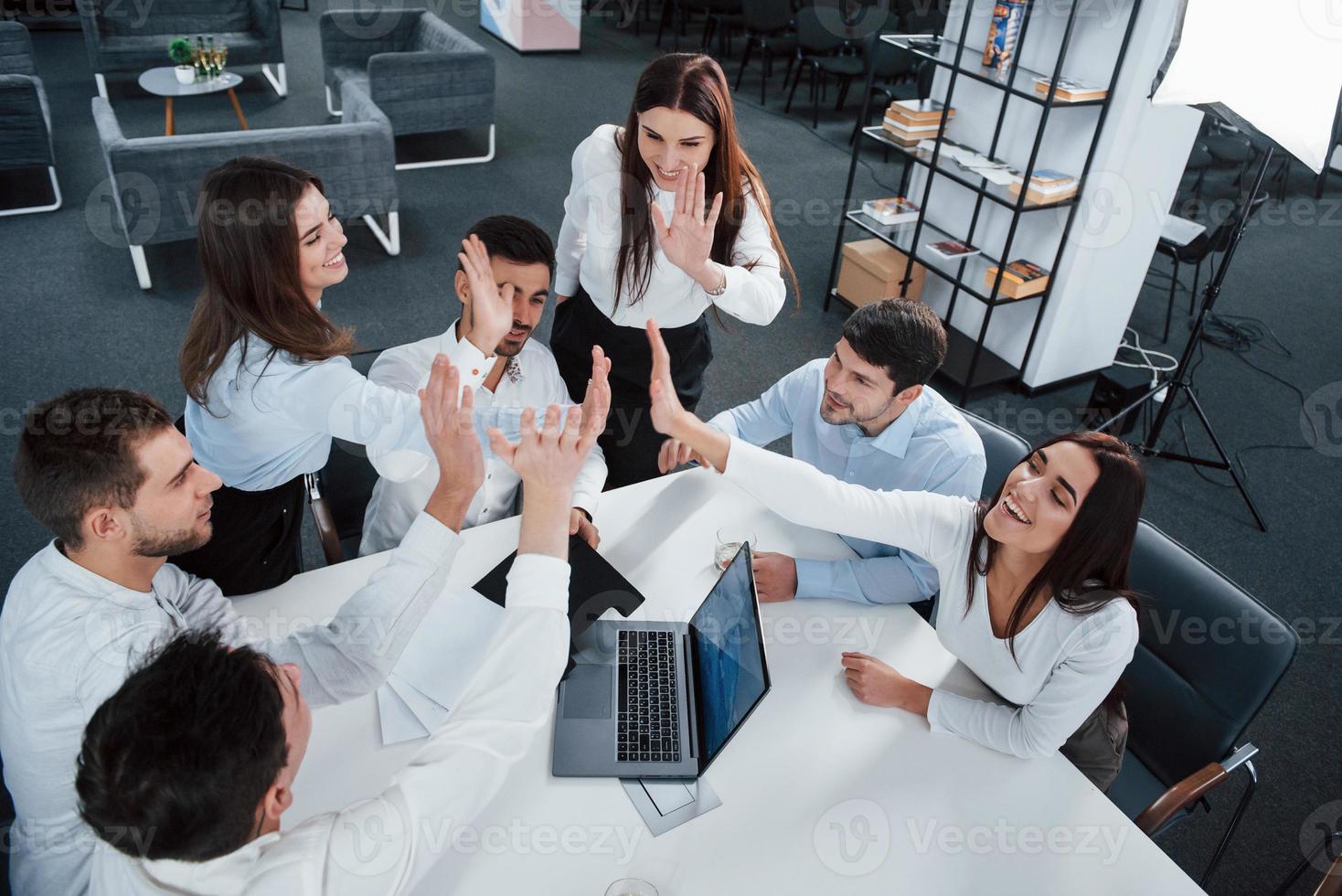 Giving high five to each other. Top view of office workers in classic wear sitting near the table using laptop and documents photo