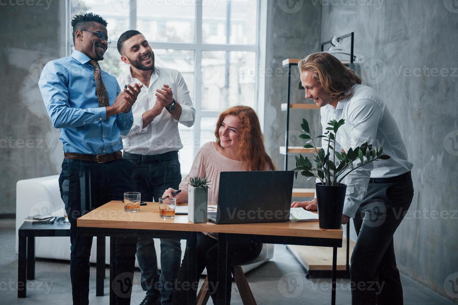 trabajadores felices. Equipo de jóvenes empresarios trabajando en un proyecto con un portátil en la mesa y sonriendo foto