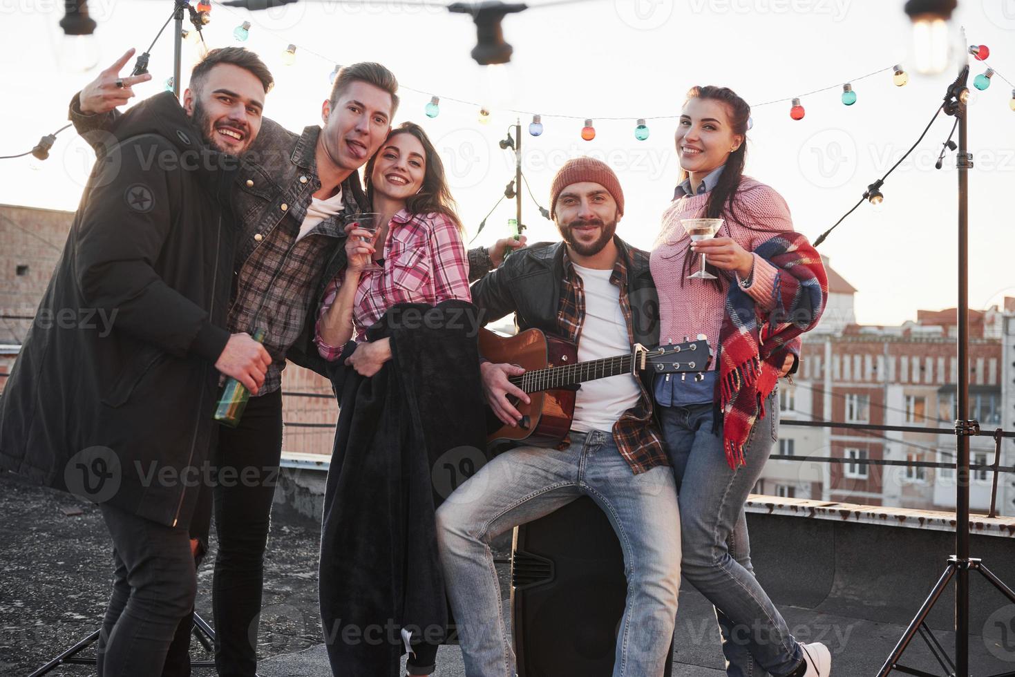 Calm and cheerful. Party at the rooftop. Five good looking friends that posing for the picture with alcohol and guitar photo