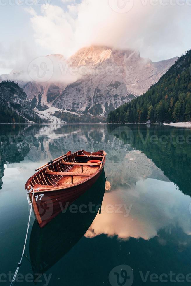 Vertical photo. Wooden boat on the crystal lake with majestic mountain behind. Reflection in the water photo
