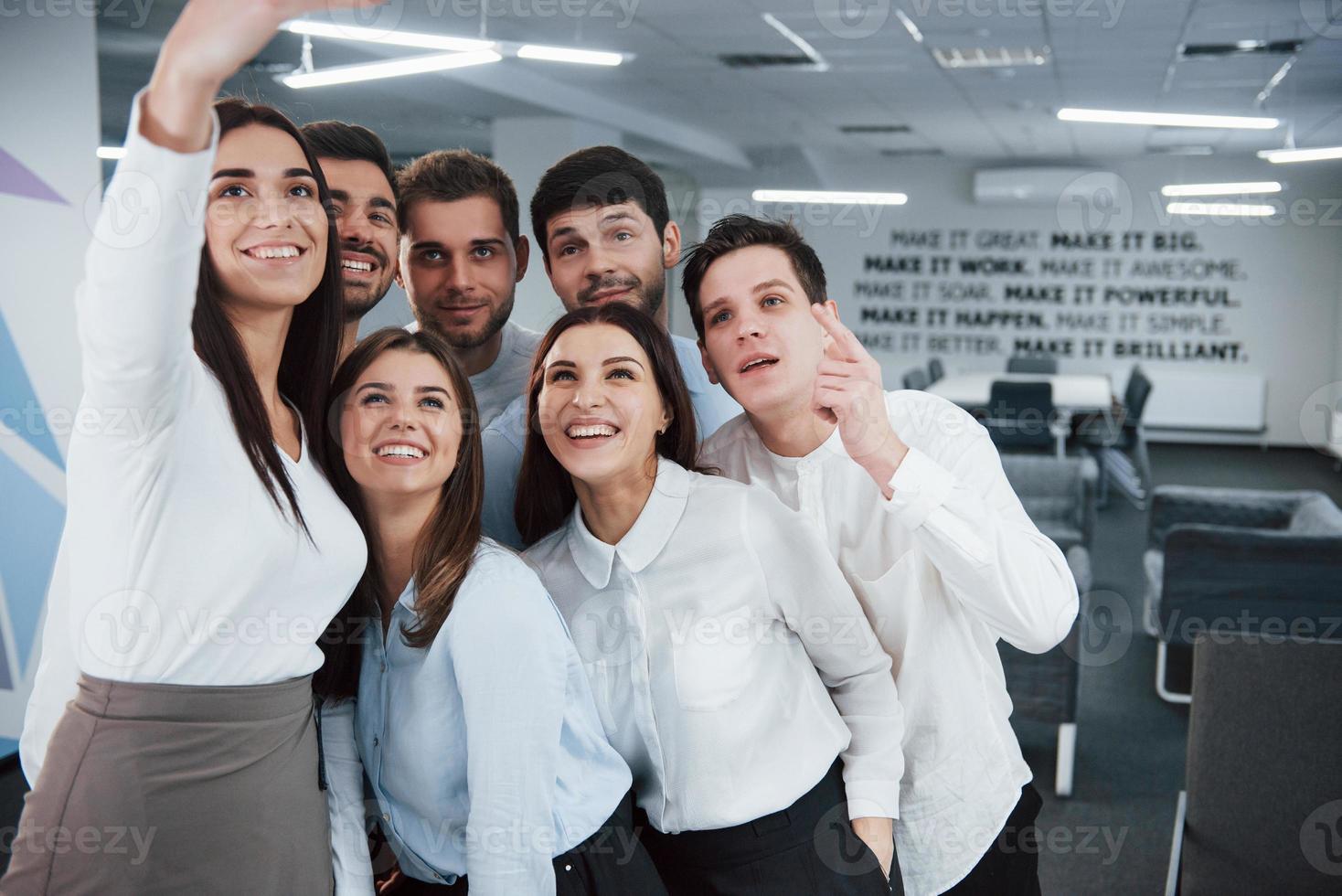 mirando a la cámara. Equipo joven haciendo selfie en ropa clásica en la moderna oficina bien iluminada foto