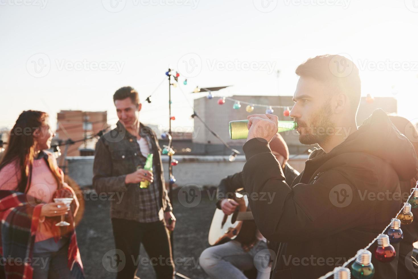 Rooftop party. Friends with alcohol having good time. Guy playing guitar photo