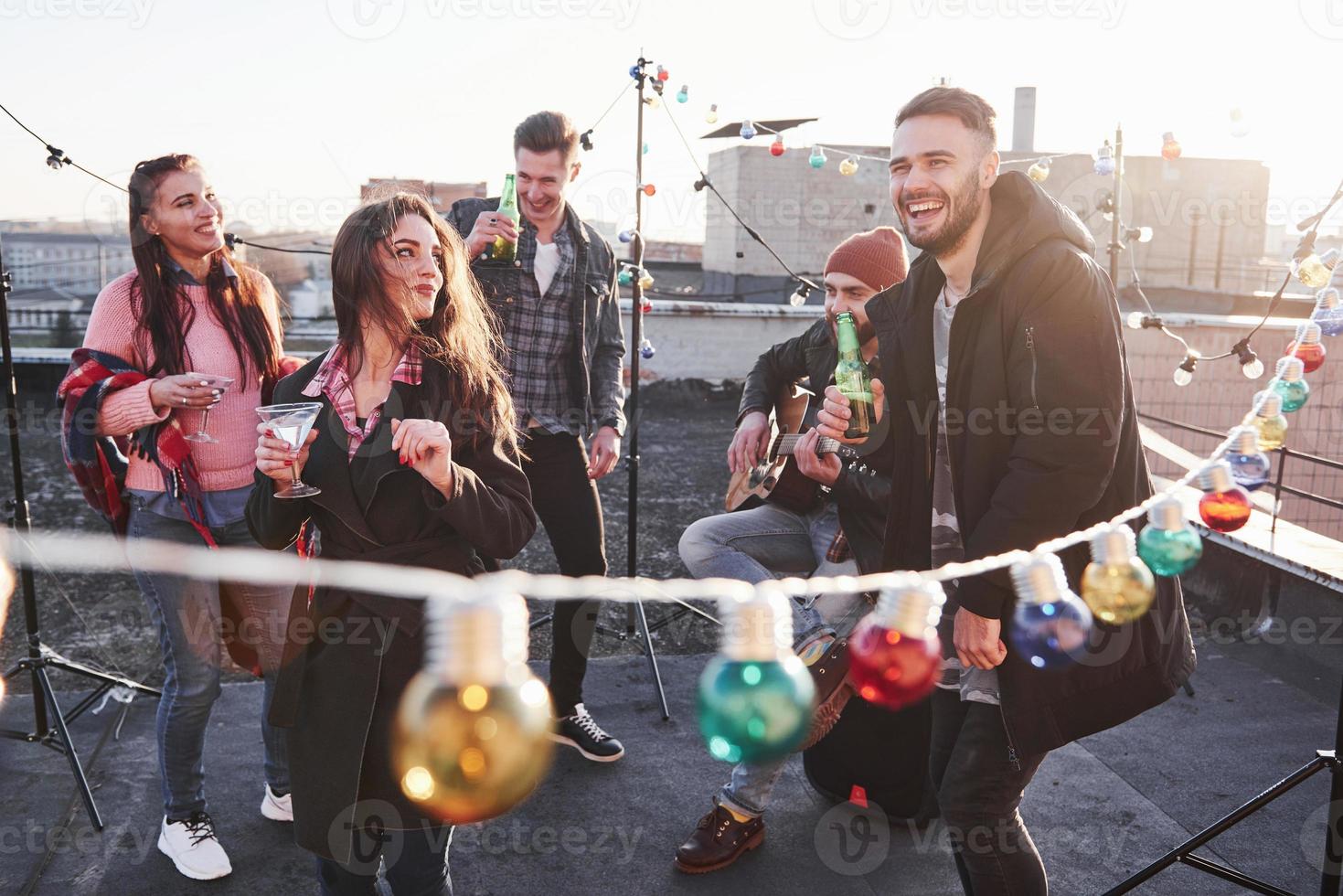 Sincere emotions. Light bulbs all around the place on the rooftop where is young group of friends have decided spend their weekend with guitar and alcohol photo