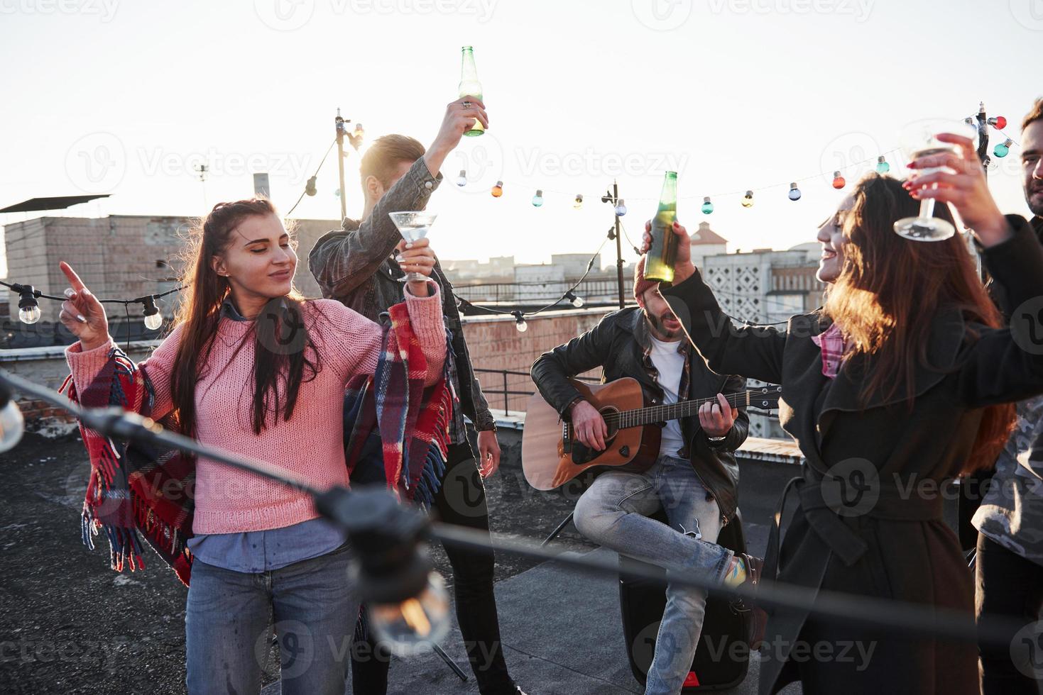 Happy young life. Group of young people having celebration at a rooftop with some alcohol and guitar playing photo