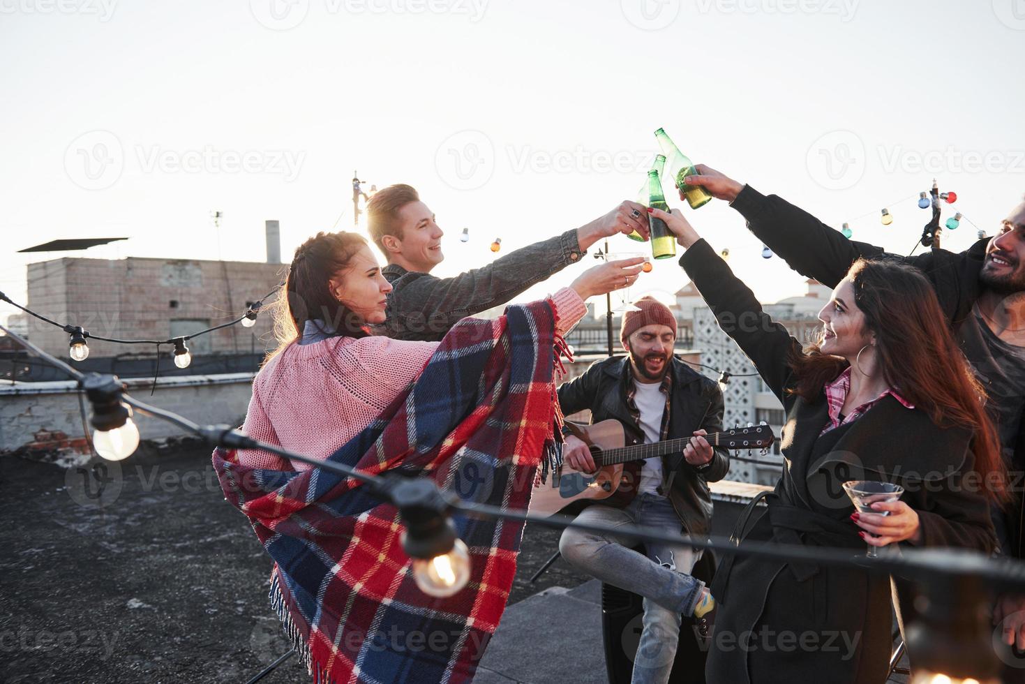 For the happiness. Group of young people having celebration at a rooftop with some alcohol and guitar playing photo