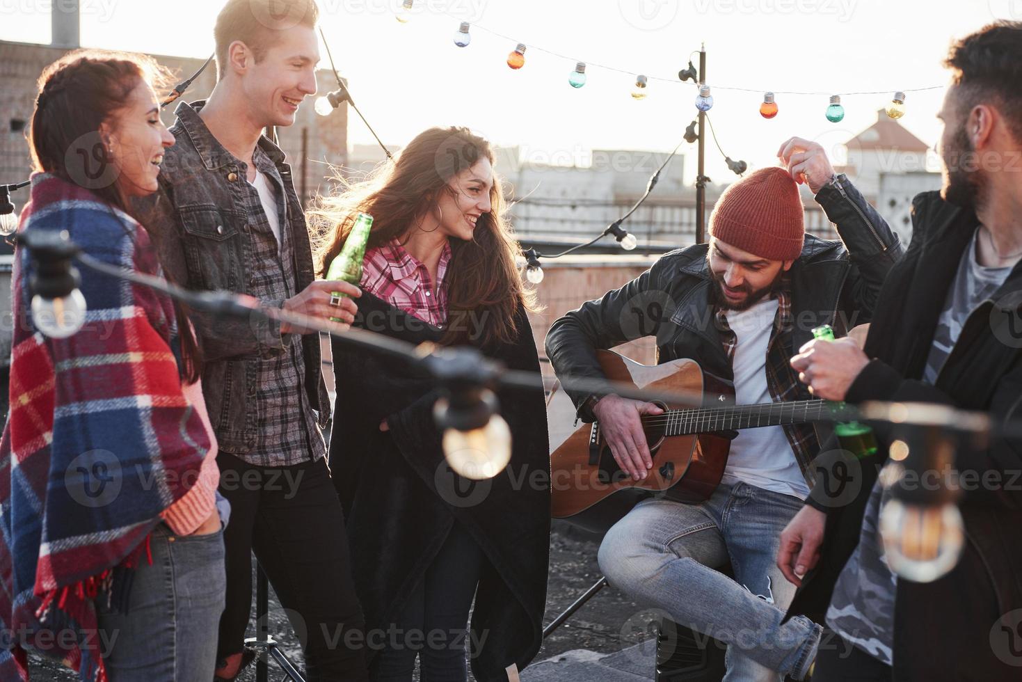 Guy in red hat tells something. Rooftop party with alcohol and acoustic guitar at sunny autumn day photo