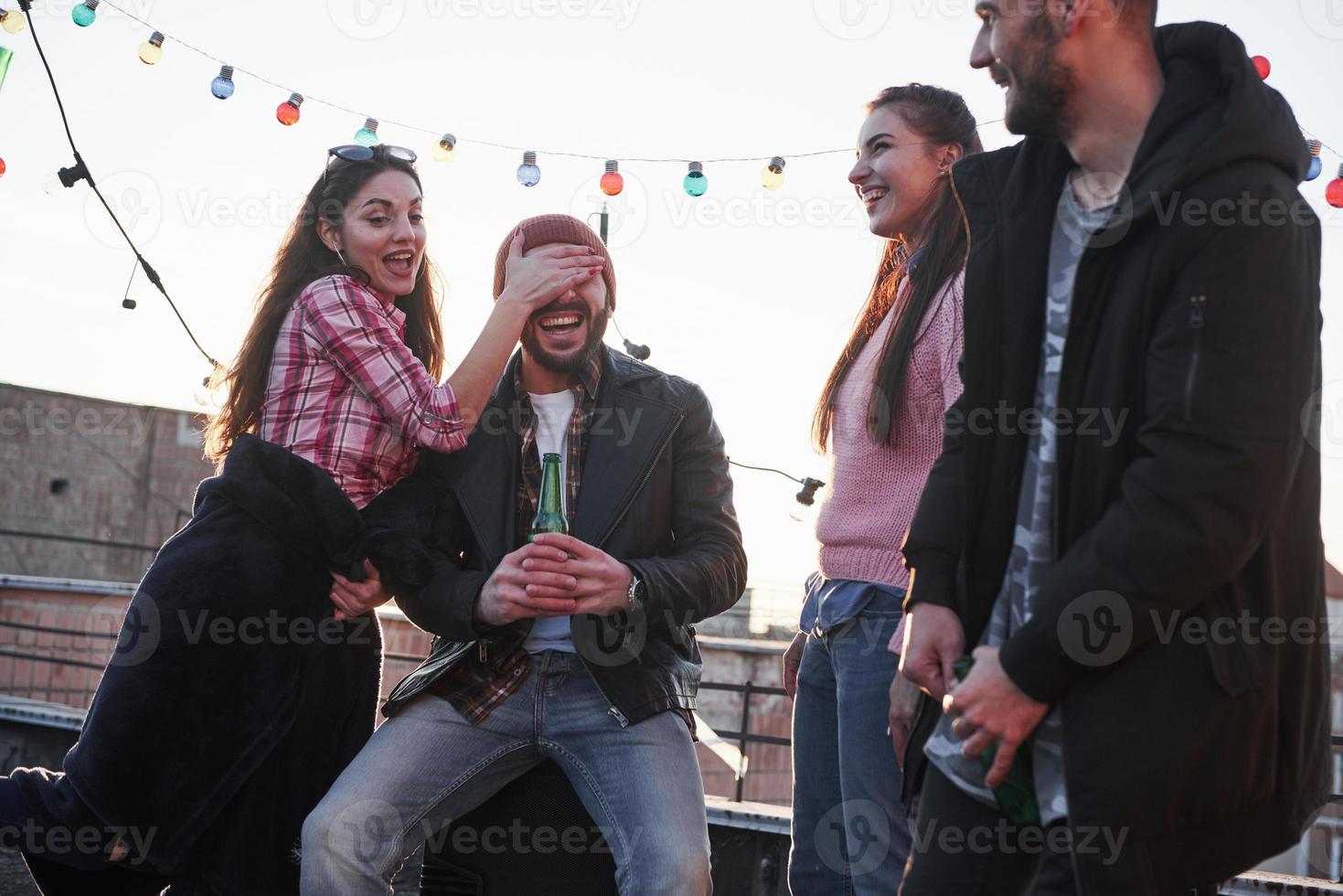Young couple having fun with friends on the rooftop. Girl covers guy's face photo
