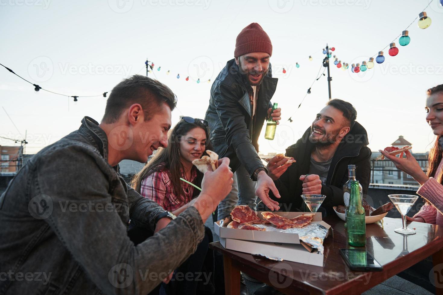Give him one more slice. Eating pizza at the rooftop party. Good friends have weekend with some delicious food and alcohol photo