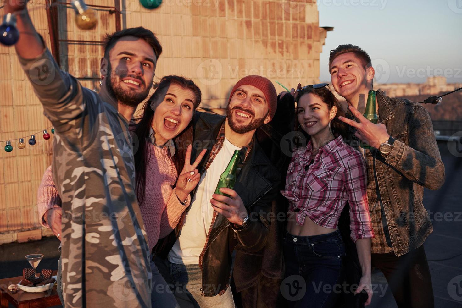 Gestures for the picture. Selfie time for group of positive friends stands on the rooftop with wall behind photo
