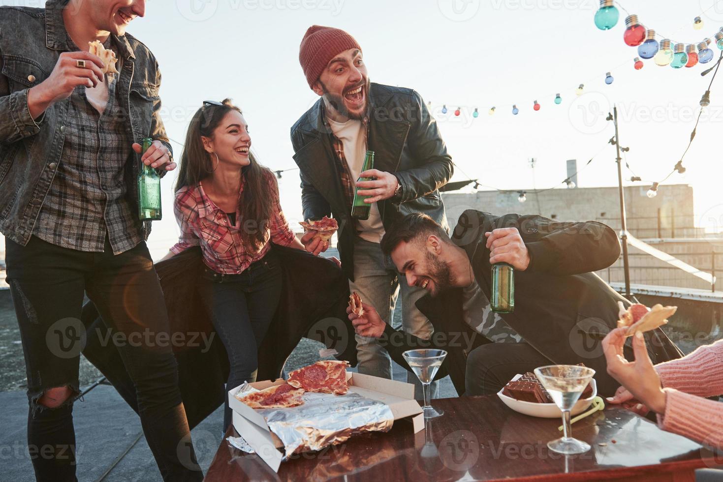 Wide smiles. Eating pizza at the rooftop party. Good friends have weekend with some delicious food and alcohol photo