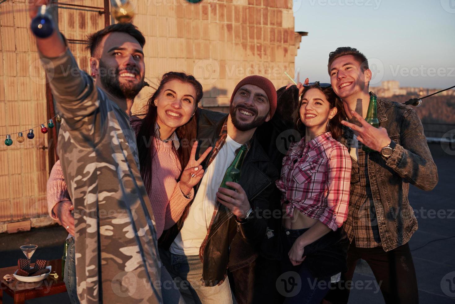 Lovely sunny weather. Selfie time for group of positive friends stands on the rooftop with wall behind photo