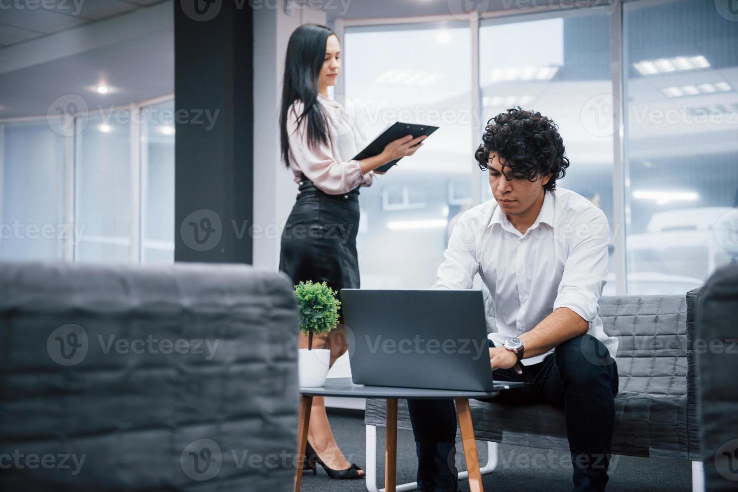 Freelance work in the office with windows behind. Two people is on their job. Guy using silver laptop. Girl read document photo