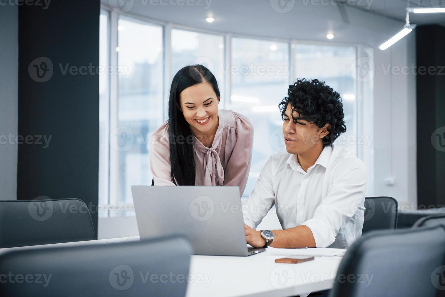 jóvenes diseñadores. Compañeros de trabajo alegres en una oficina moderna sonriendo al hacer su trabajo usando la computadora portátil foto