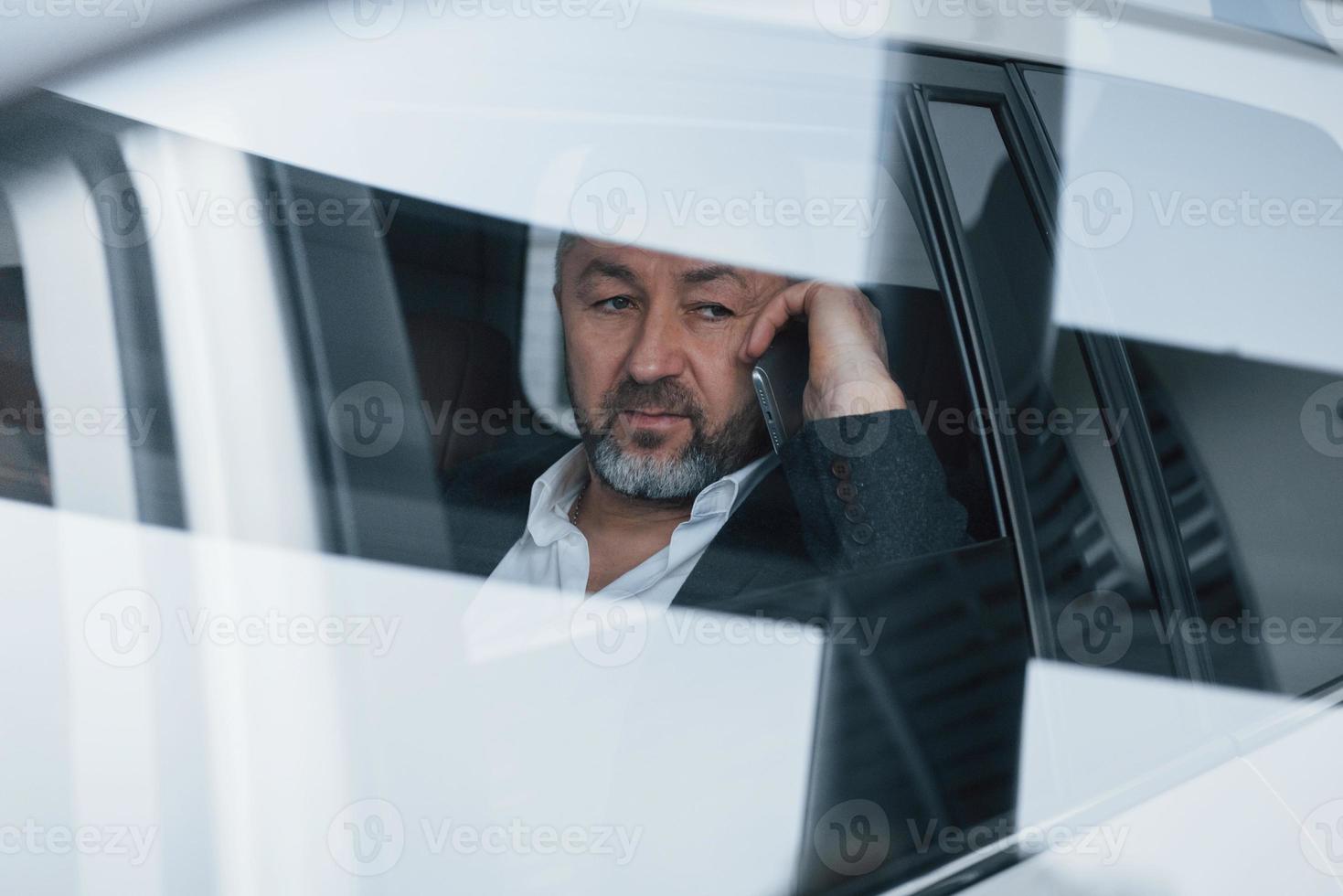 Seems tired. Reflection on window. Having business call while sitting at the back of modern luxury car photo