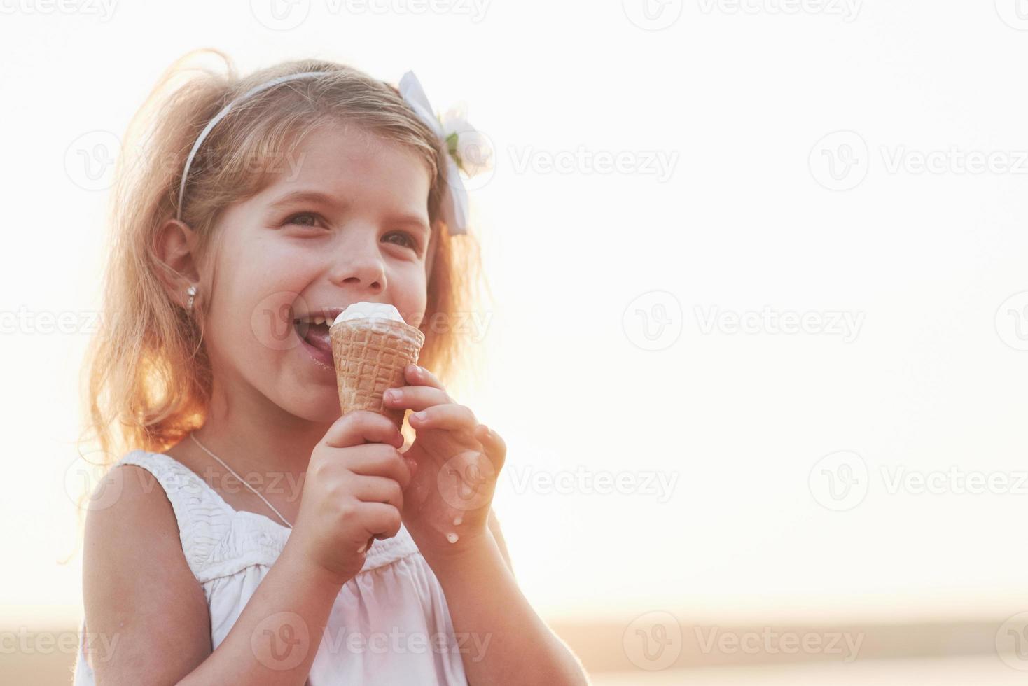 Cute smiling little girl eating ice cream at background of lake and woods photo