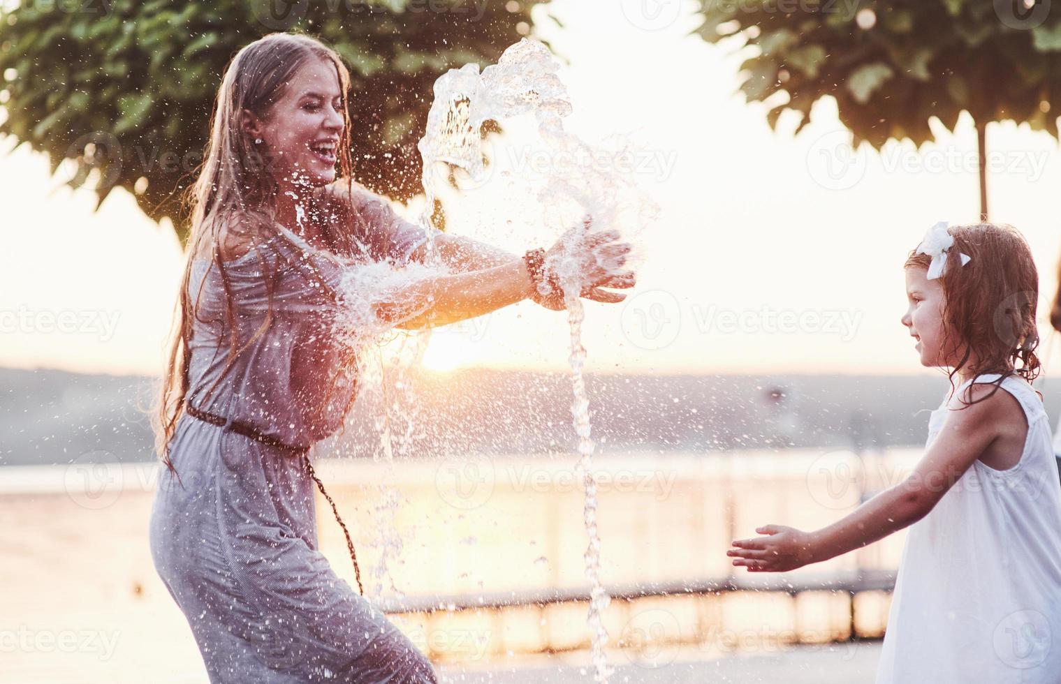 Catch the water. In a hot sunny day mother and her daughter decide to use fountain for cooling themselves and have fun with it photo