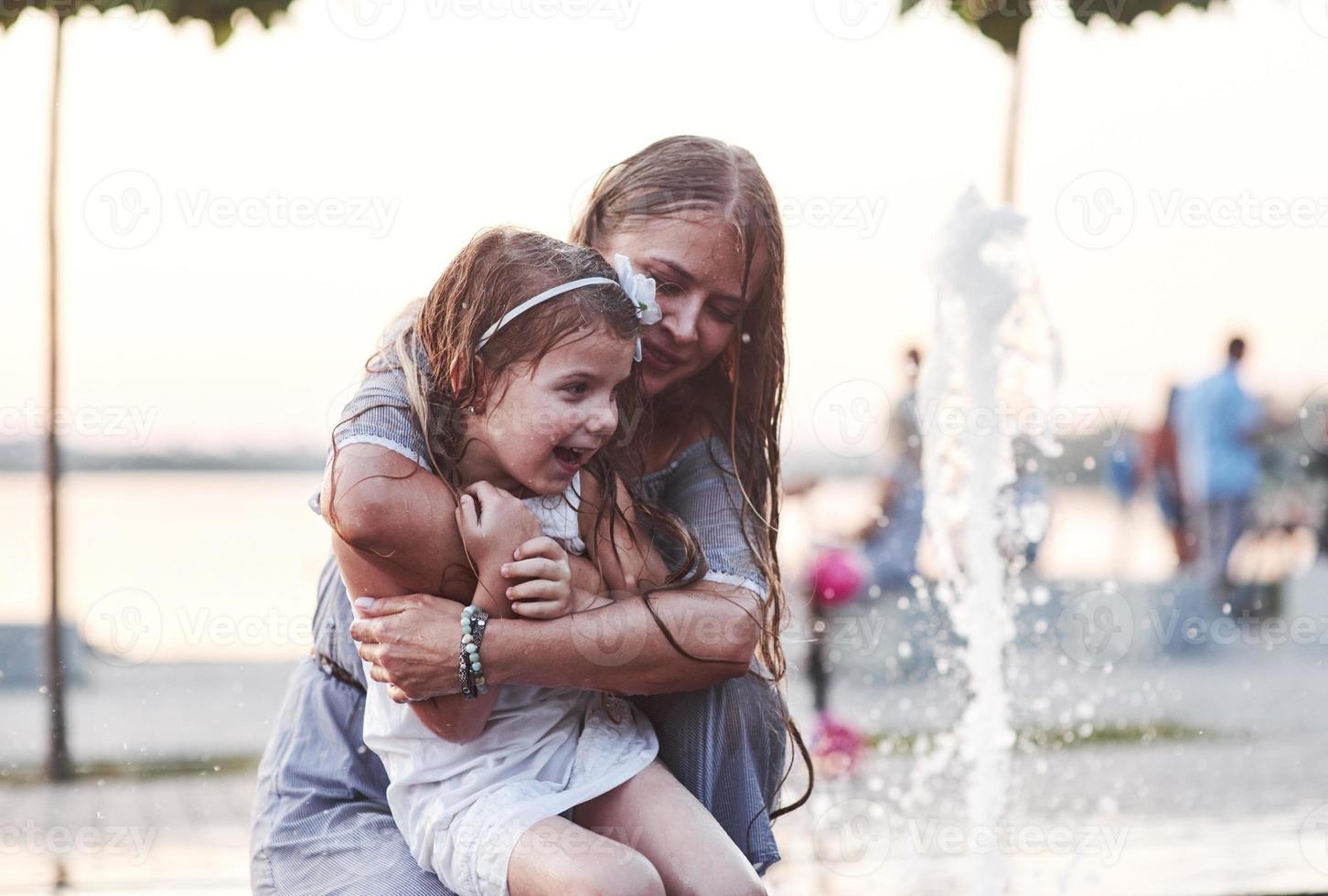 Childish curiosity. In a hot sunny day mother and her daughter decide to use fountain for cooling themselves and have fun with it photo