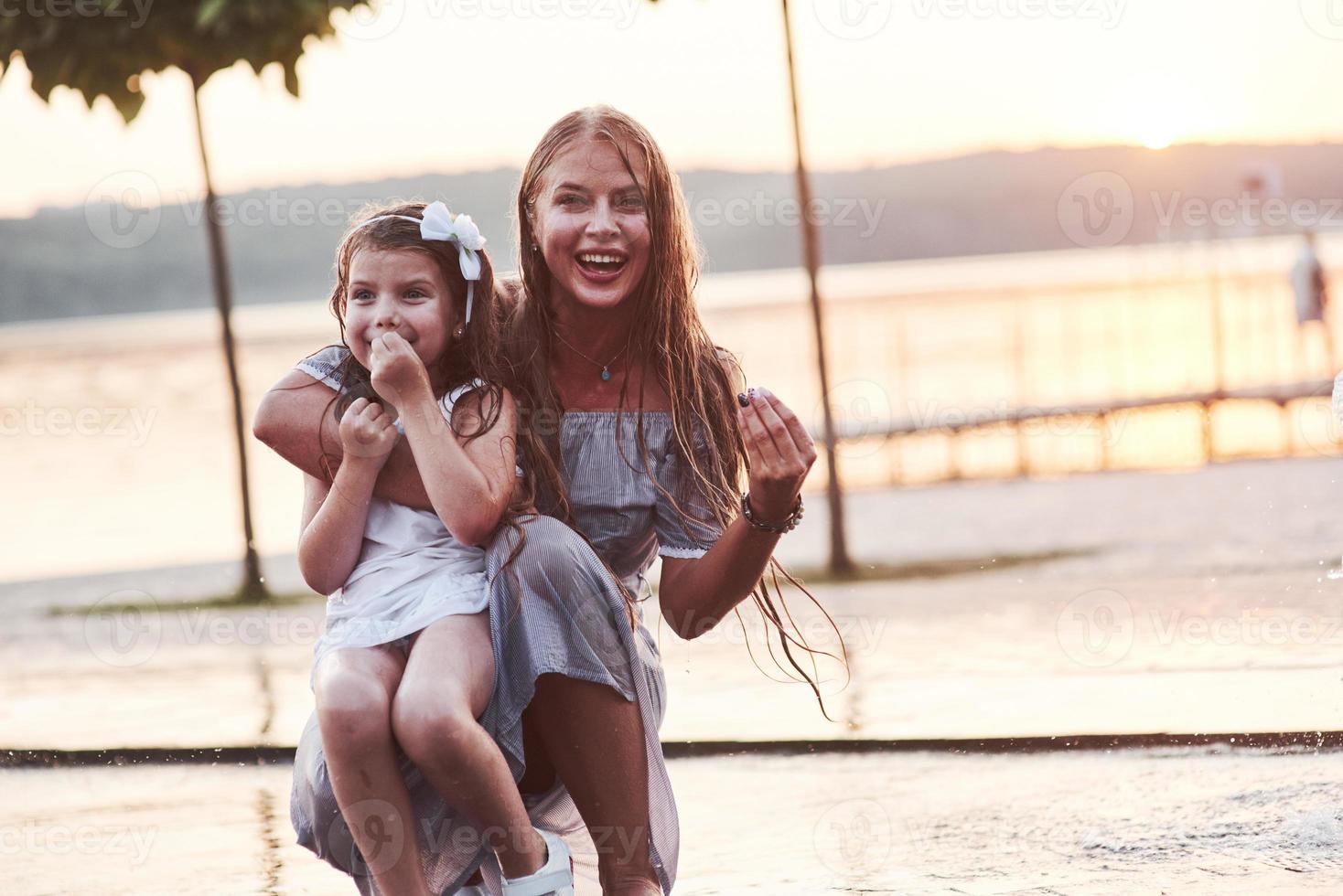 sonriendo por la foto. en un día caluroso y soleado, la madre y su hija deciden usar la fuente para refrescarse y divertirse con ella foto