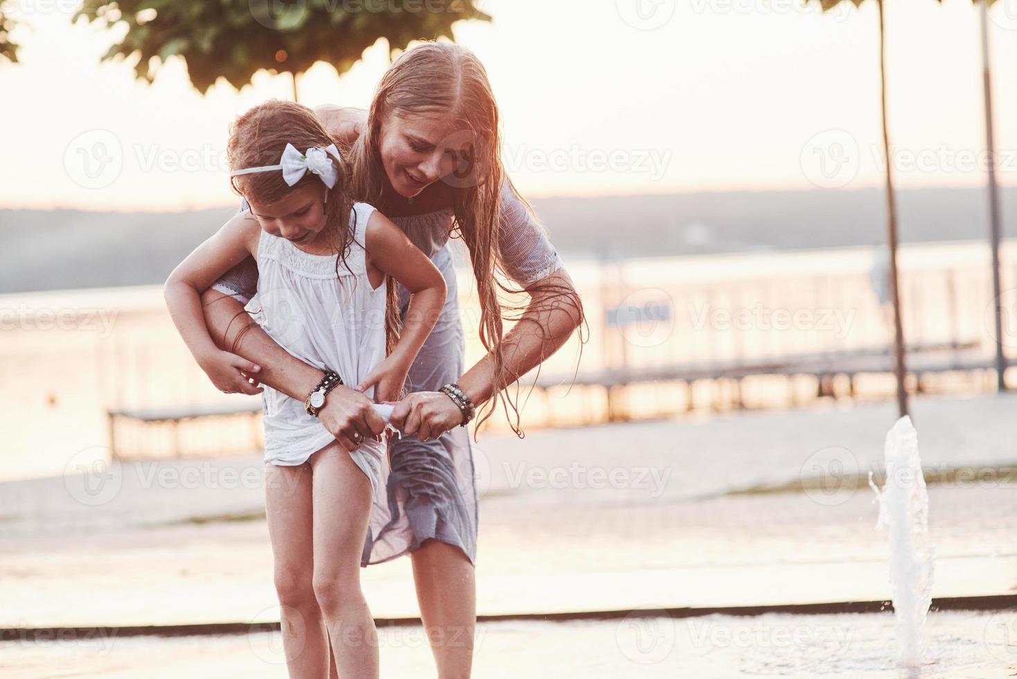apretando un vestido. en un día caluroso y soleado, la madre y su hija deciden usar la fuente para refrescarse y divertirse con ella foto
