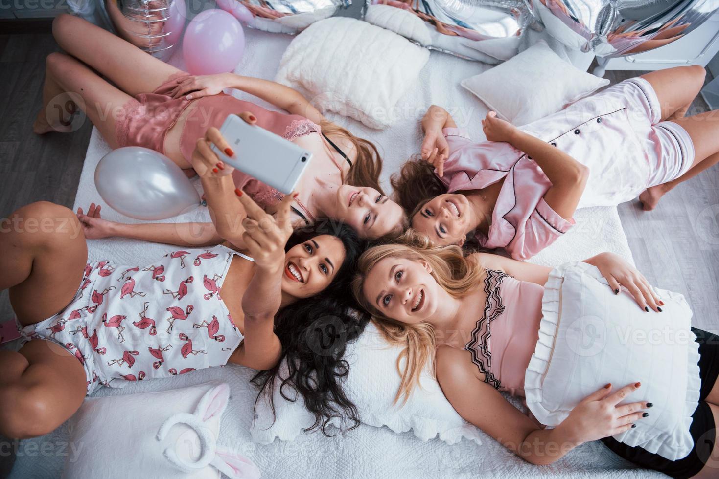 disfruta reunirse. tomando selfie con amigos mientras está acostado en la cama en la despedida de soltera foto