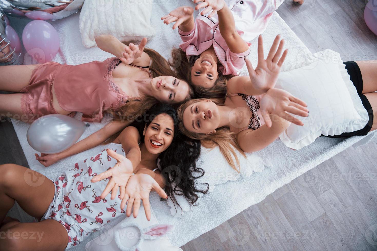 Top view of young girls at bachelorette party lying on the sofa and raising their hands up photo