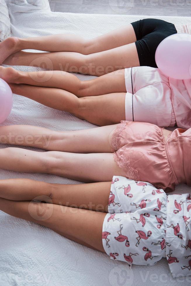 buena piel tersa. foto vertical. las chicas jóvenes acostadas en la cama blanca de lujo tienen celebrando. vista superior