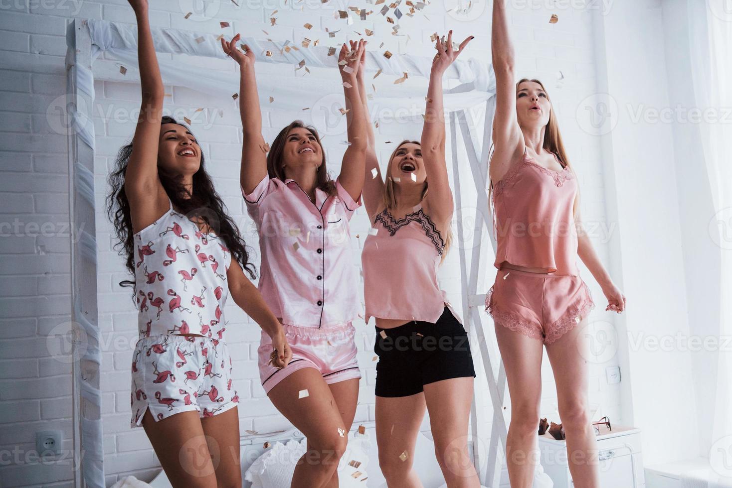Raise up hands as high as possible Confetti in the air. Young girls have fun on the white bed in nice room photo